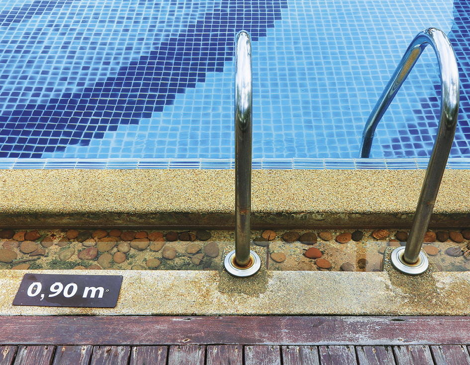 Fotografia. Parte externa de uma piscina, com destaque para a escada à direita e uma placa à esquerda escrita: 0 vírgula 90 metro.