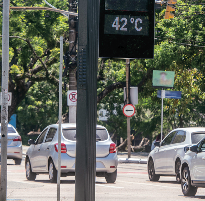 Fotografia. Destaque para um relógio em uma rua marcando 42 graus Celsius. Ao lado, carros e árvores.