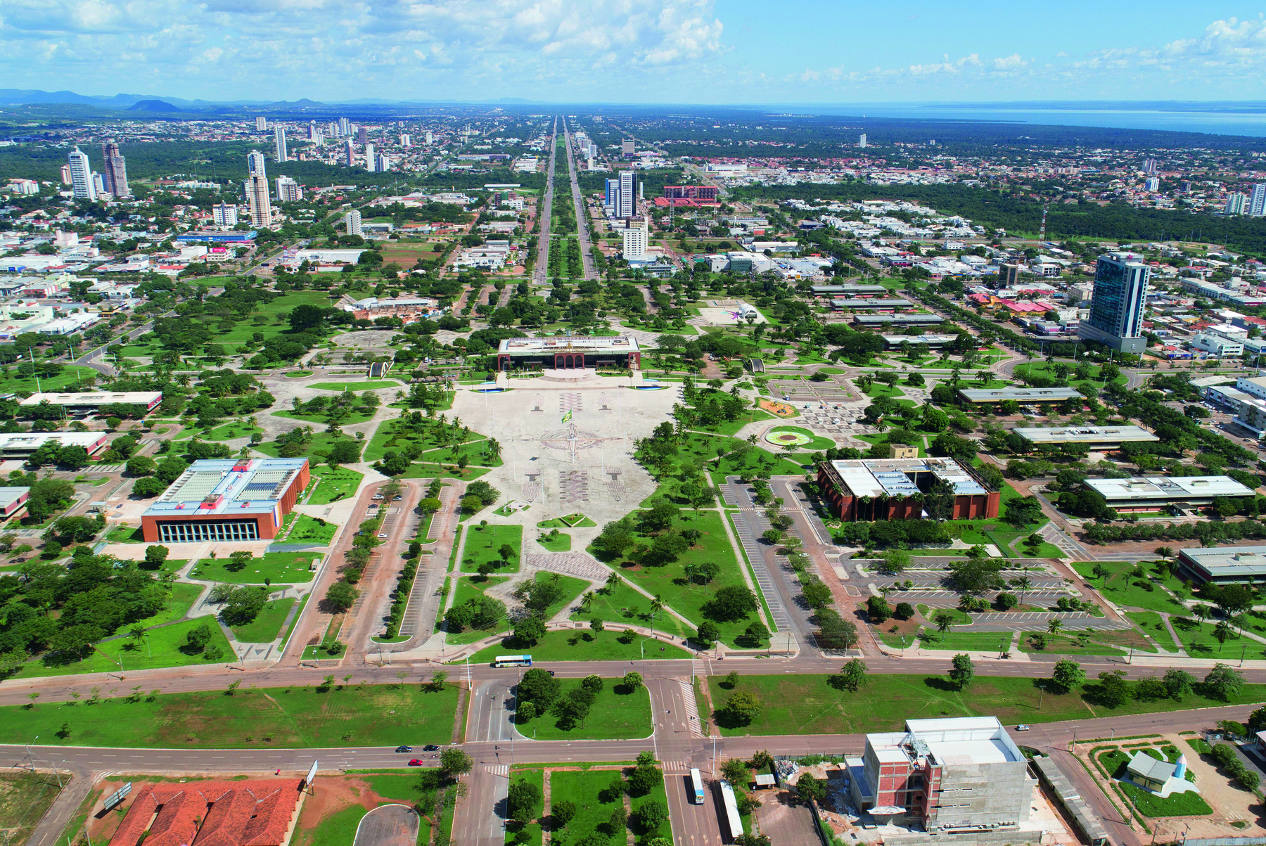 Fotografia. Visão de parte de uma área de Palmas em Tocantins. Região plana com ruas verticais e horizontais. Há construções e pouca vegetação.