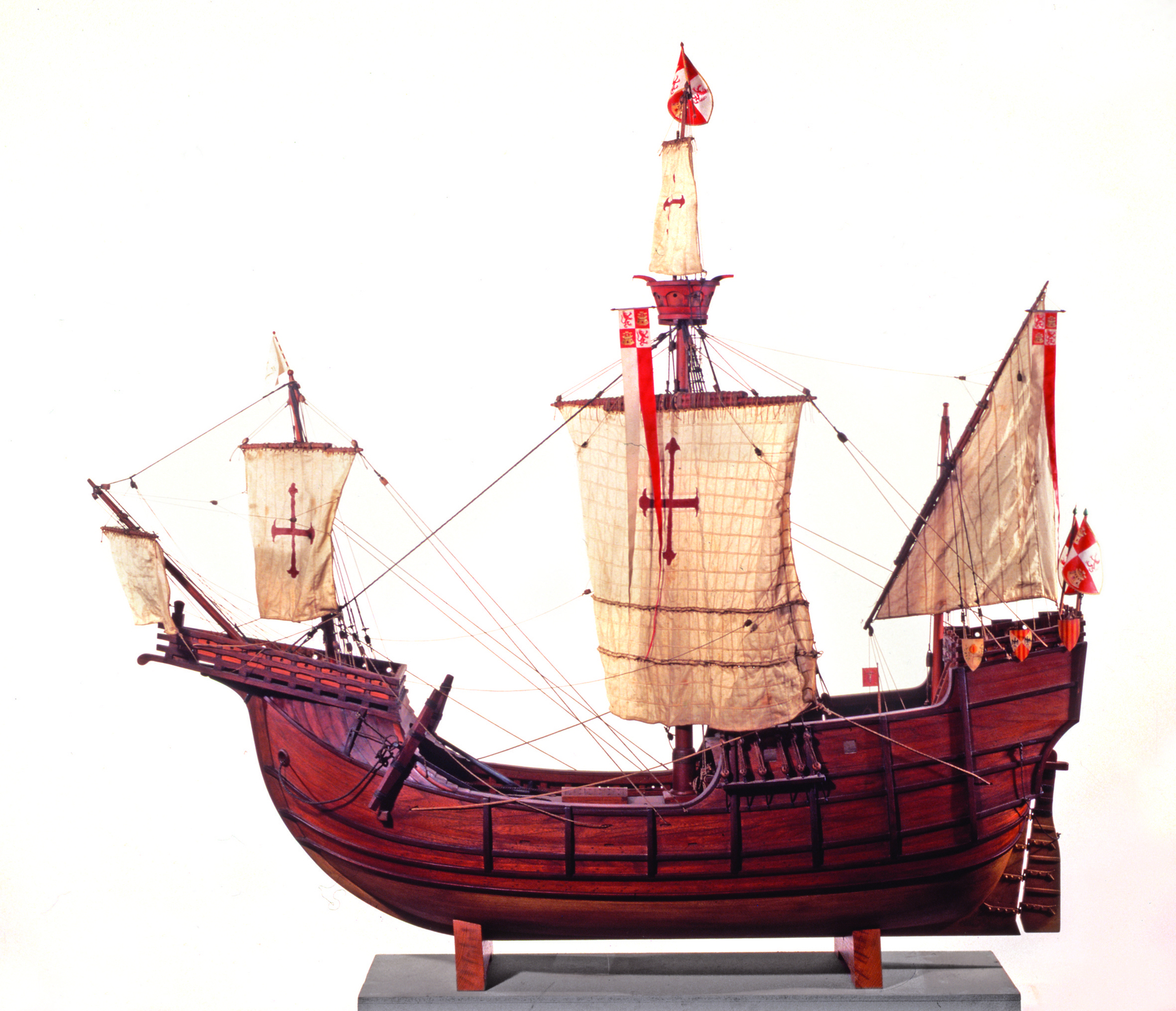 Ilustração: Um barco a velas. O casco do barco é marrom, e as velas são bege com um símbolo vermelho que se assemelha a uma cruz.