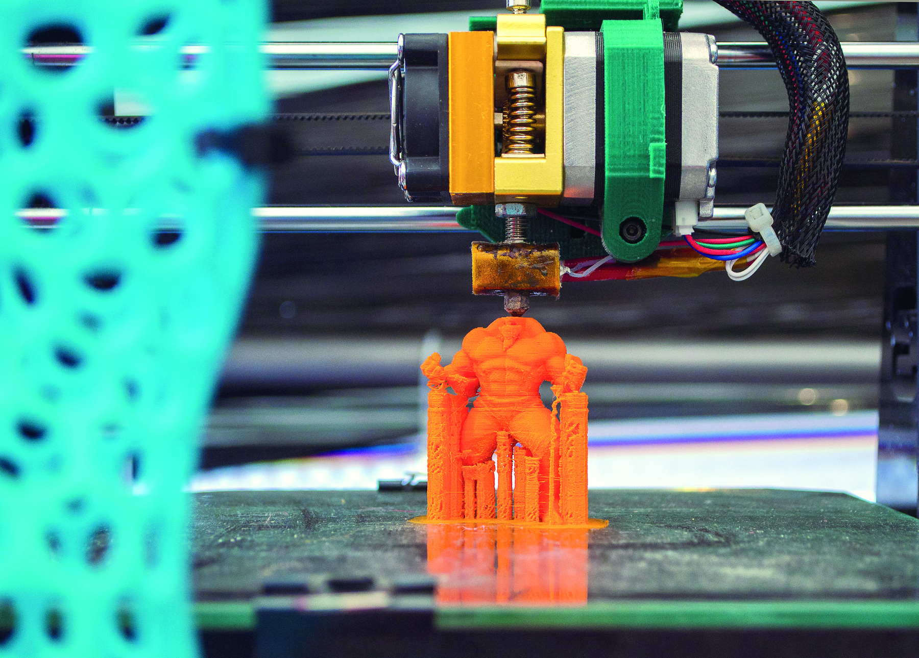 Fotografia: Impressora 3D está imprimindo um boneco laranja, estilo super-herói.
