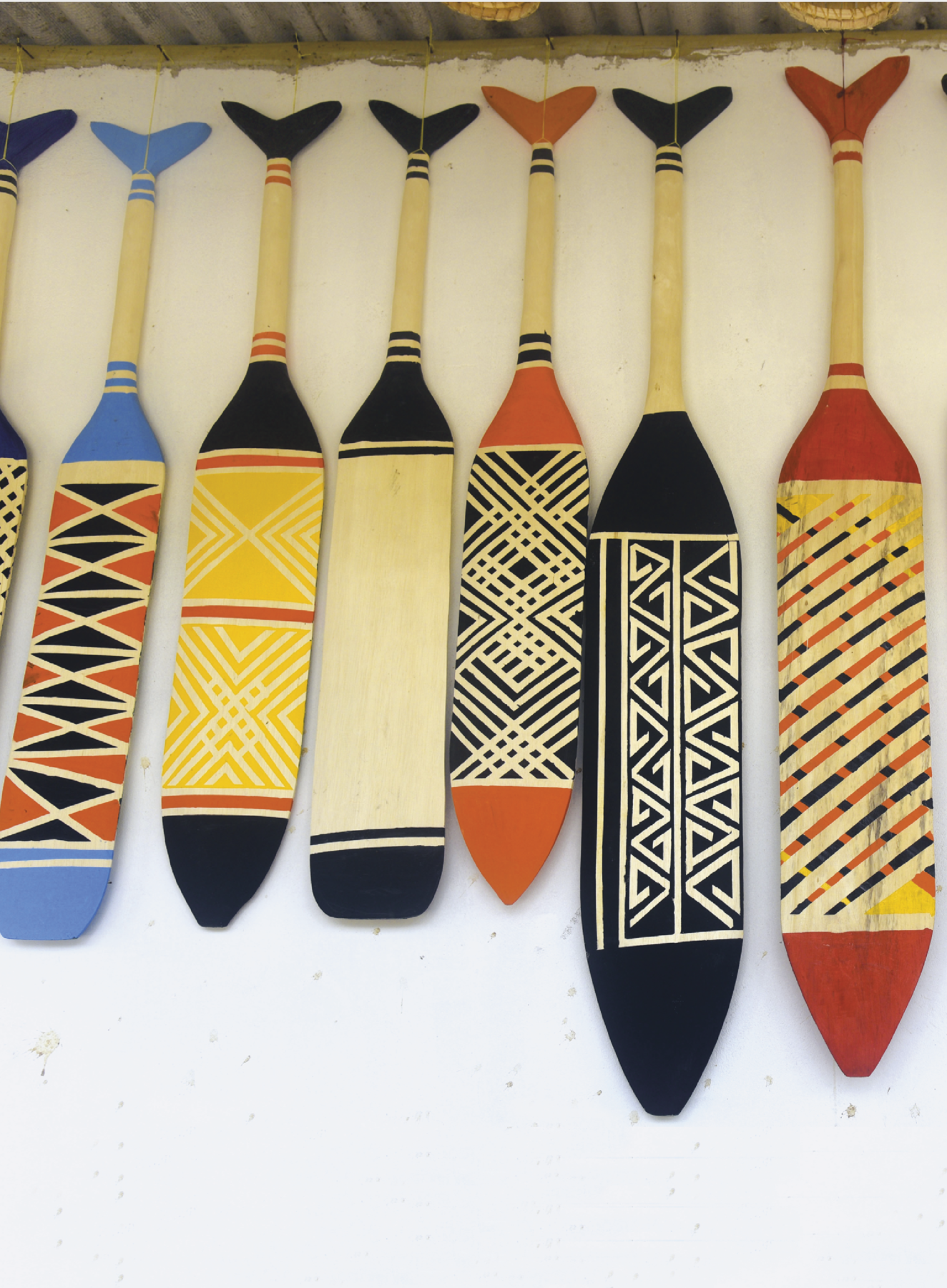 Fotografia. Seis remos de madeira cada um pintado com um tipo de grafismo indígena.