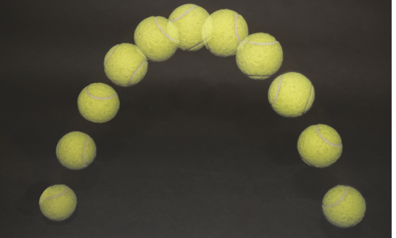 Fotografia. Diversos registros de uma bola de tênis na mesma imagem, com o fundo preto. A sequência de fotos forma uma trajetória semelhante de uma parábola, parecida com a letra u de cabeça para baixo.