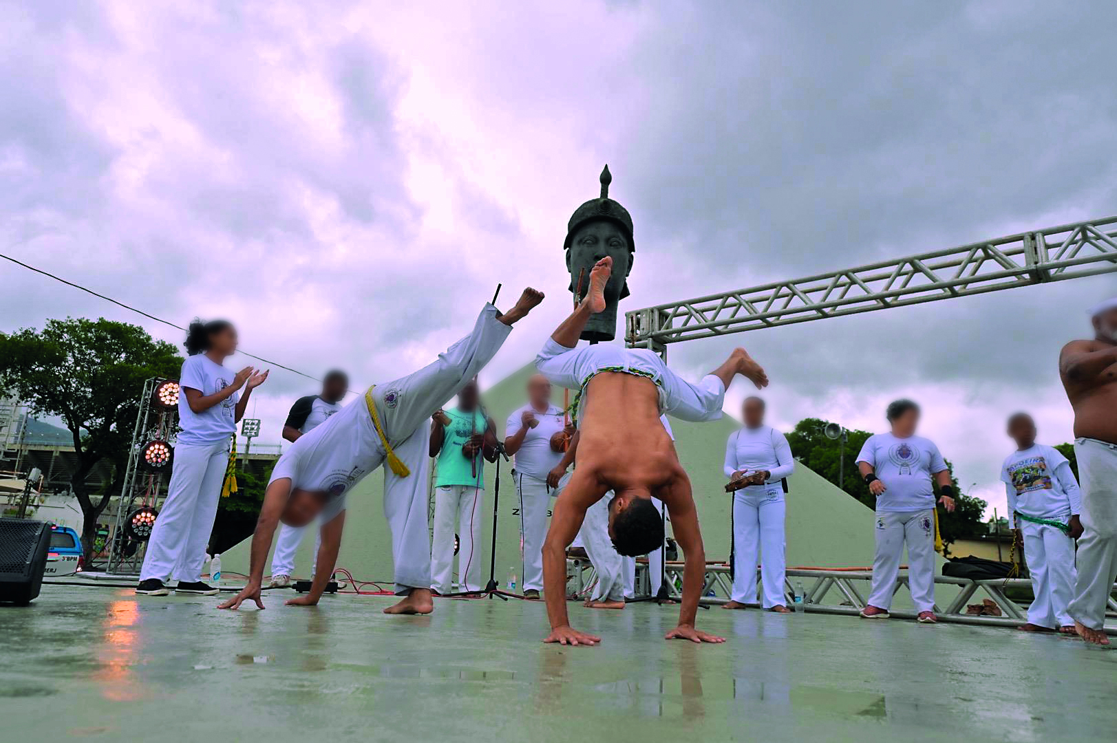 Fotografia. Grupo de pessoas jogando capoeira na frente de um monumento histórico.