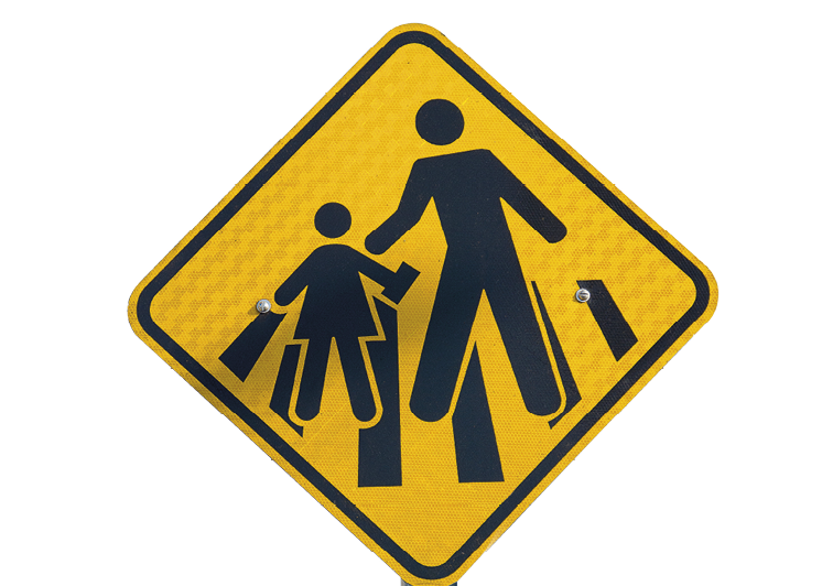Fotografia. Placa em formato de losango amarelo. Dentro, representação de um adulto e uma criança sobre faixa de pedestres.
