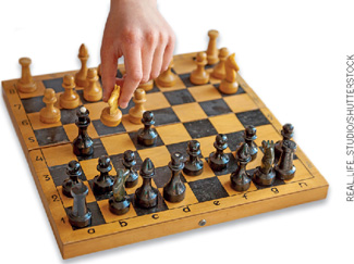 IMAGEM: uma mão move uma peça clara em um tabuleiro de xadrez. FIM DA IMAGEM.
