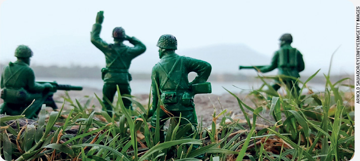 IMAGEM: quatro soldados de brinquedo colocados sobre a grama. eles são verdes, usam capacetes e estão de costas. três seguram armas, enquanto o quarto está no centro com um dos braços erguido. FIM DA IMAGEM.