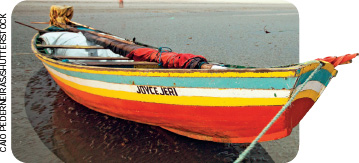 IMAGEM: uma canoa ancorada em uma praia. a canoa é pintada com listras e no casco está escrito joyce jeri. longos remos estão colocados dentro da embarcação, que também possui assentos feitos com tábuas. FIM DA IMAGEM.