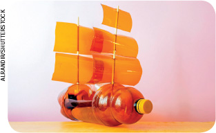 IMAGEM: um navio feito com sucata. a estrutura da embarcação é uma garrafa plástica colocada na horizontal; os mastros são palitos de madeira e as velas são pedaços de plástico. FIM DA IMAGEM.