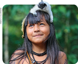 IMAGEM: uma menina indígena com um pequeno macaco sobre sua cabeça. FIM DA IMAGEM.