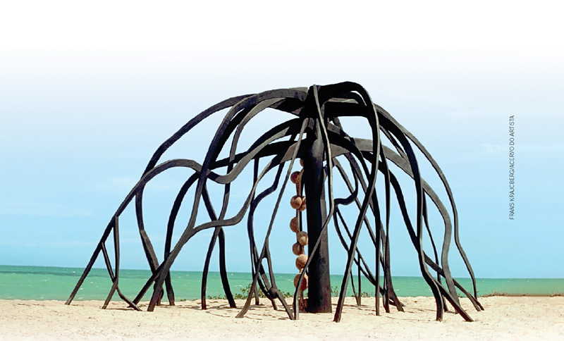IMAGEM: escultura a flor do mangue, de frans krajcberg, em uma praia. a obra é composta por pedaços de madeira que lembram um coqueiro com folhas que tocam a areia. FIM DA IMAGEM.