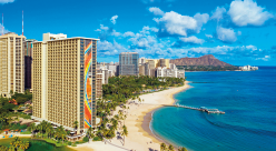 IMAGEM: fotografia da praia de Waikiki, com prédios e construções na beira da praia, no fundo, um grande vulcão. FIM DA IMAGEM.