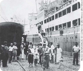 IMAGEM: fotografia em preto e branco de imigrantes no porto de santos. FIM DA IMAGEM.
