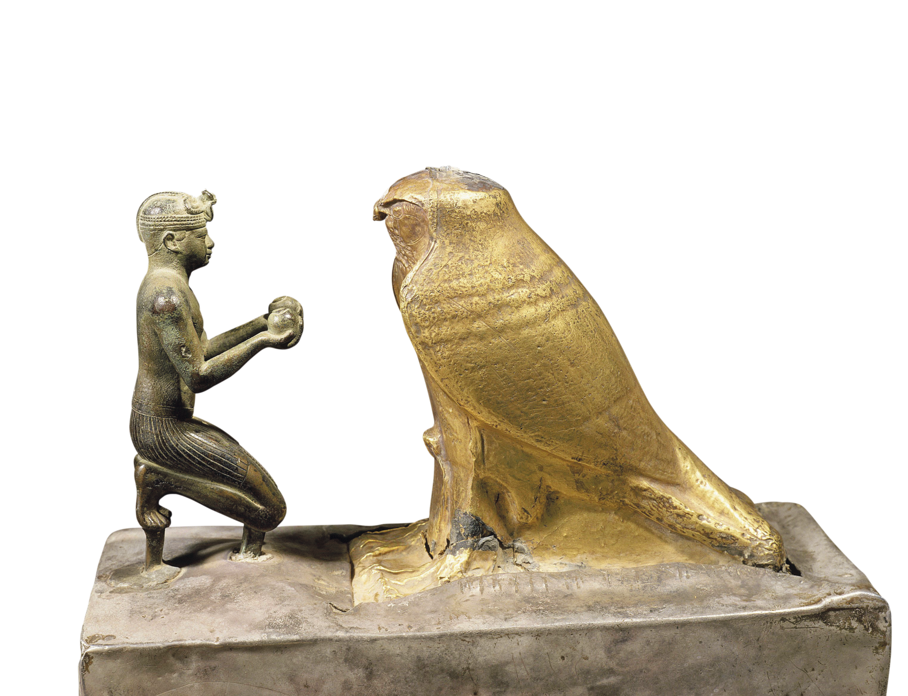 Estatueta. Escultura metálica representando um homem ajoelhado, segurando objetos redondos com as mãos, em direção a um grande falcão dourado a sua frente.