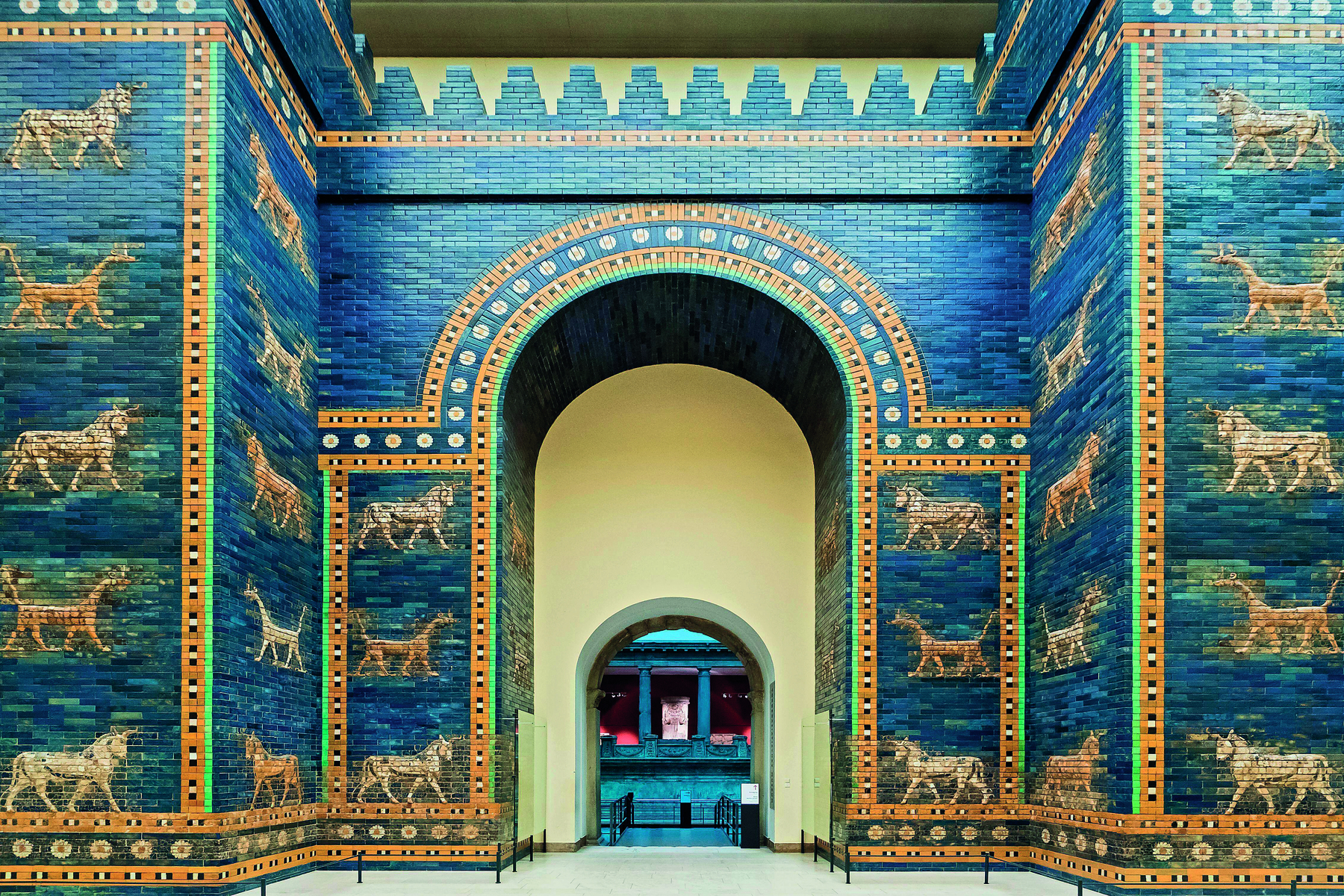 Fotografia. Vista da entrada de uma construção, com paredes azuis e imagens de animais dourados. No centro, uma grande abertura com formato arqueado no topo.