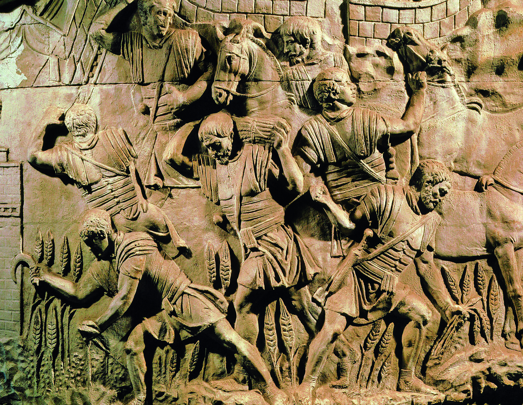 Relevo. Homens vestindo armaduras, colhendo trigo e carregando ramos do cereal sobre suas costas, em área de plantação.