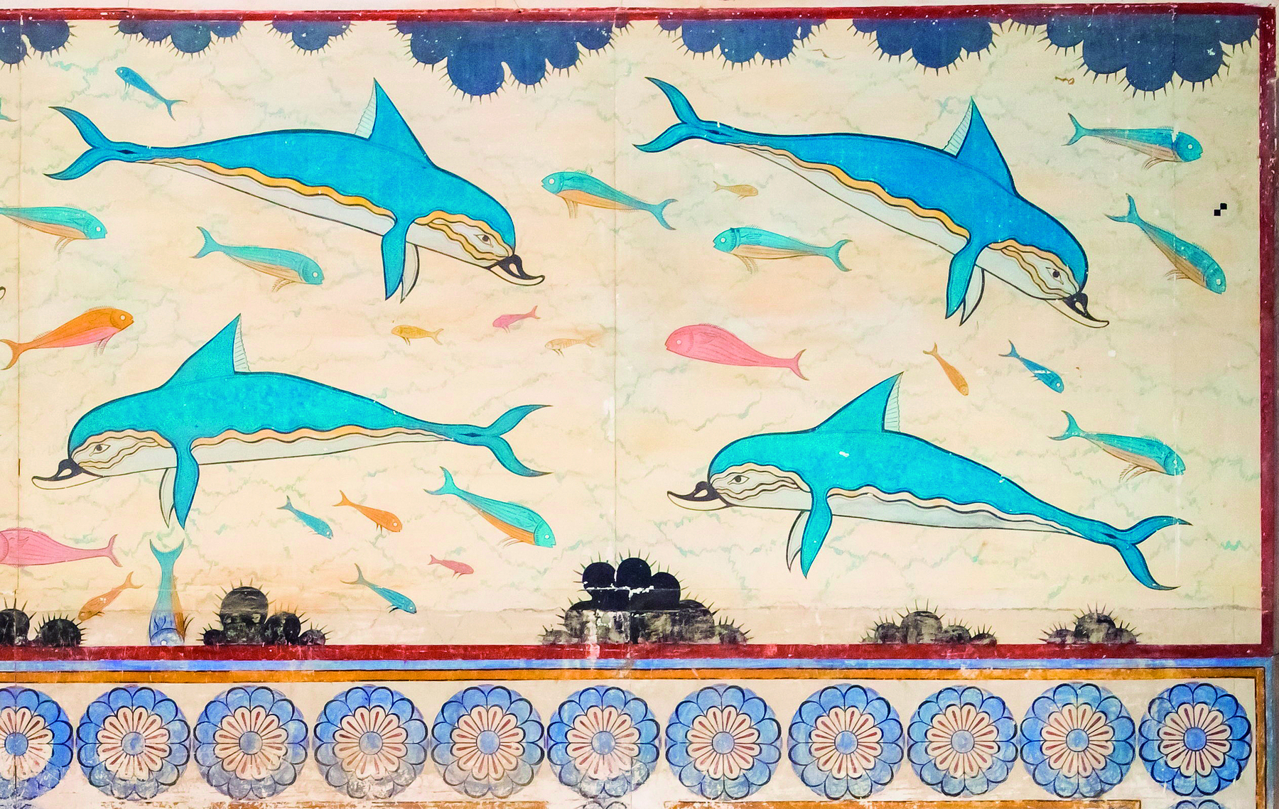 Afresco. Representação de golfinhos com nadadeiras laterais, cauda e uma nadadeira no dorso. São de coloração azul. Ao redor, peixes coloridos. Na base inferior, uma faixa horizontal com flores de pétalas azuis e miolo branco.