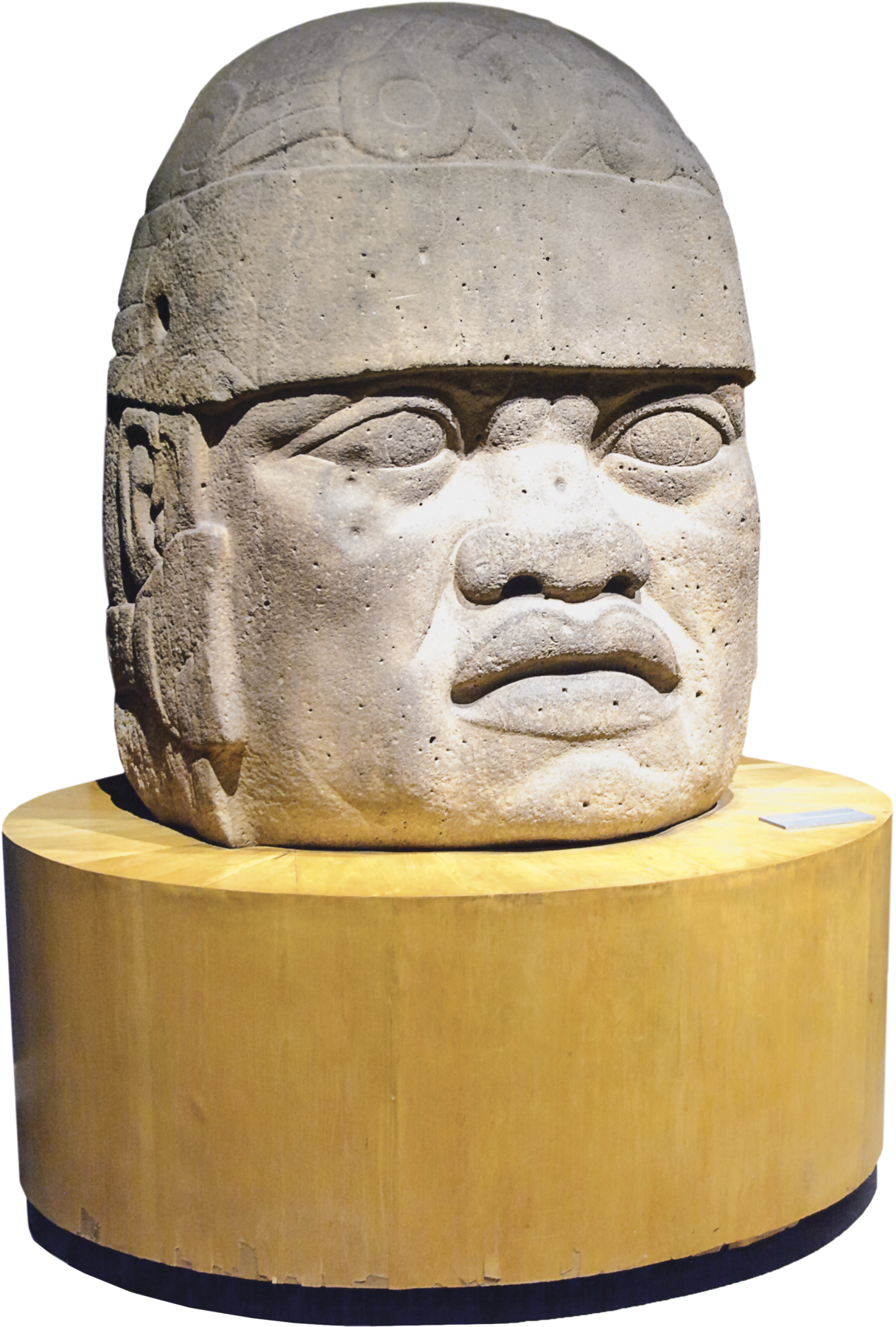 Escultura. Rosto com feições humanas sobre um suporte de madeira de formato circular. O rosto possui nariz com abas largas, lábios volumosos e um capacete ao redor da cabeça.
