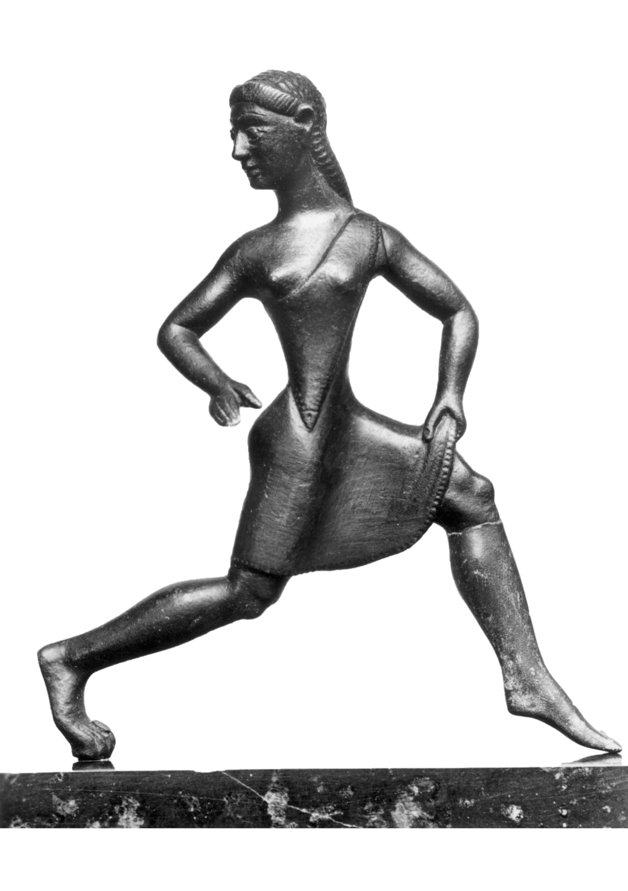 Escultura. Mulher vestindo uma túnica na altura dos joelhos, com um longo cabelo trançado. Ela está em posição de corrida, com as pernas afastadas e flexionadas, e os braços em posições contrárias.