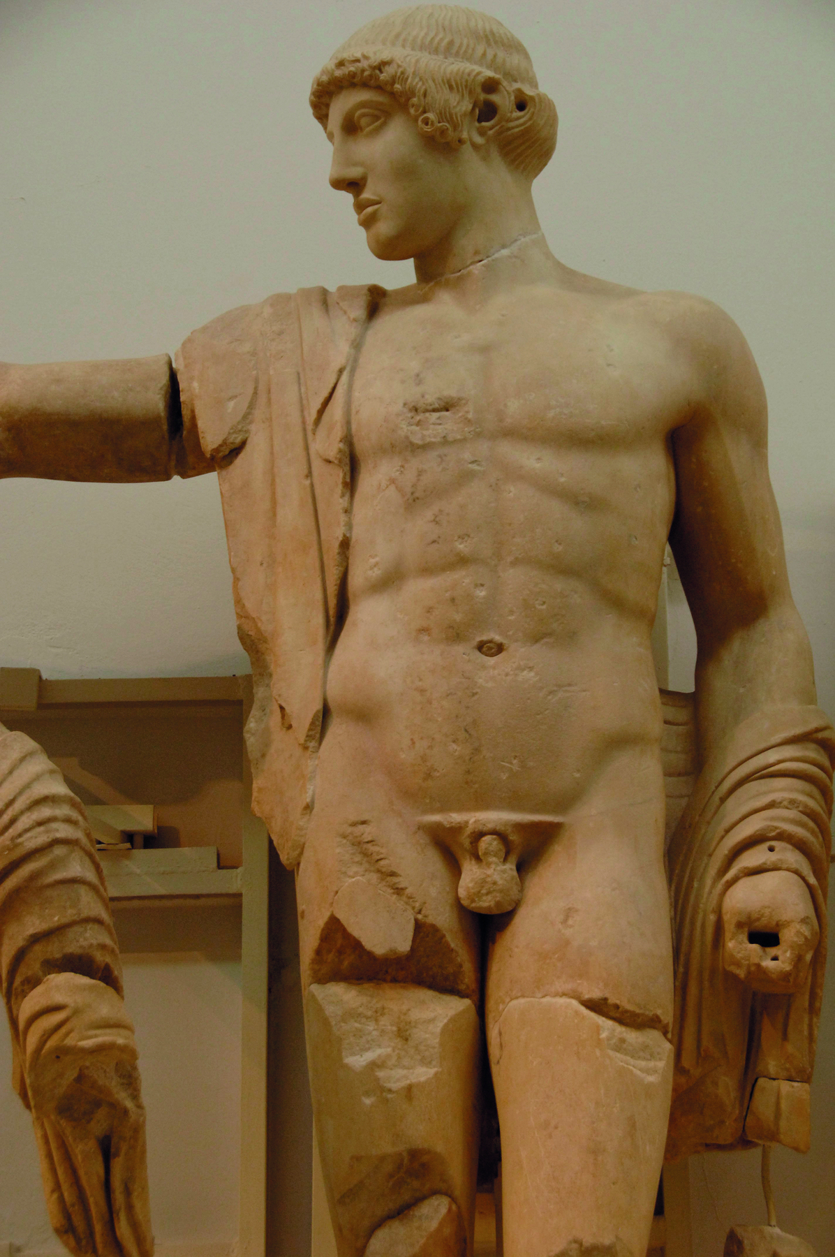 Escultura. Homem com o corpo desnudo, visto de perfil, com cabelos curtos e uma faixa de tecido sobre seu ombro.
