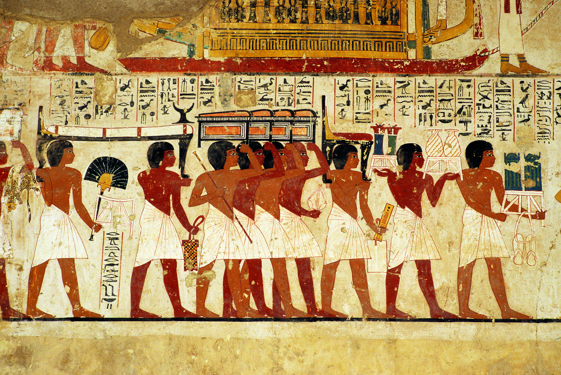 Pintura. Homens vestindo tecidos brancos ao redor de suas cinturas, lado a lado, apoiando um sarcófago em suas mãos, sobre suas cabeças. Acima, imagens de hieróglifos.