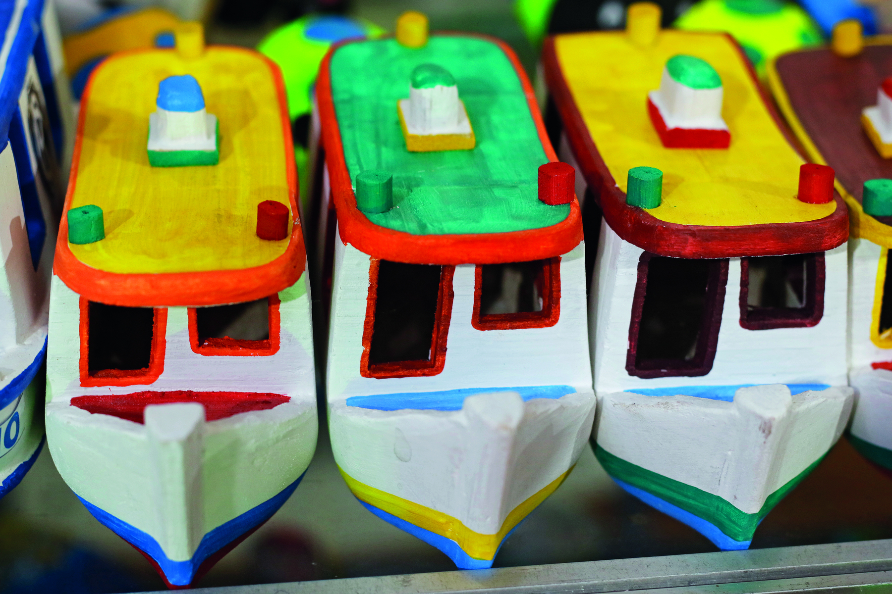 Fotografia. Três barquinhos de brinquedo, lado a lado, com cascos brancos e detalhes coloridos. À frente há uma janela e uma entrada em cada barquinho.