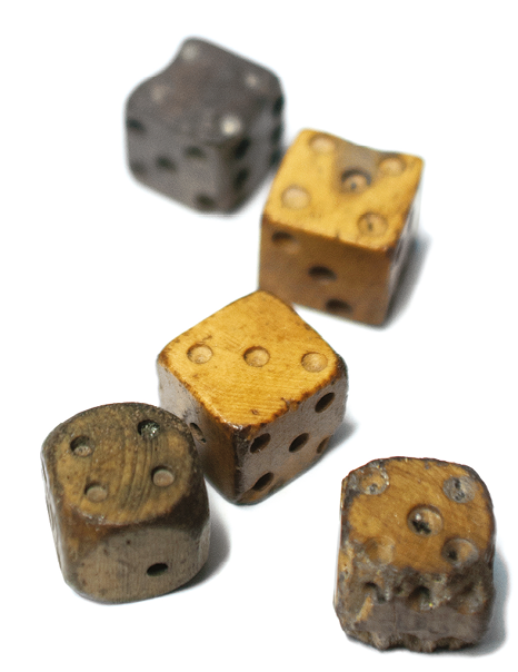 Fotografia. Cinco dados de metal, contendo pontos entalhados em cada uma de suas faces.  Um dado na cor preta, dois dourados e dois acobreados.