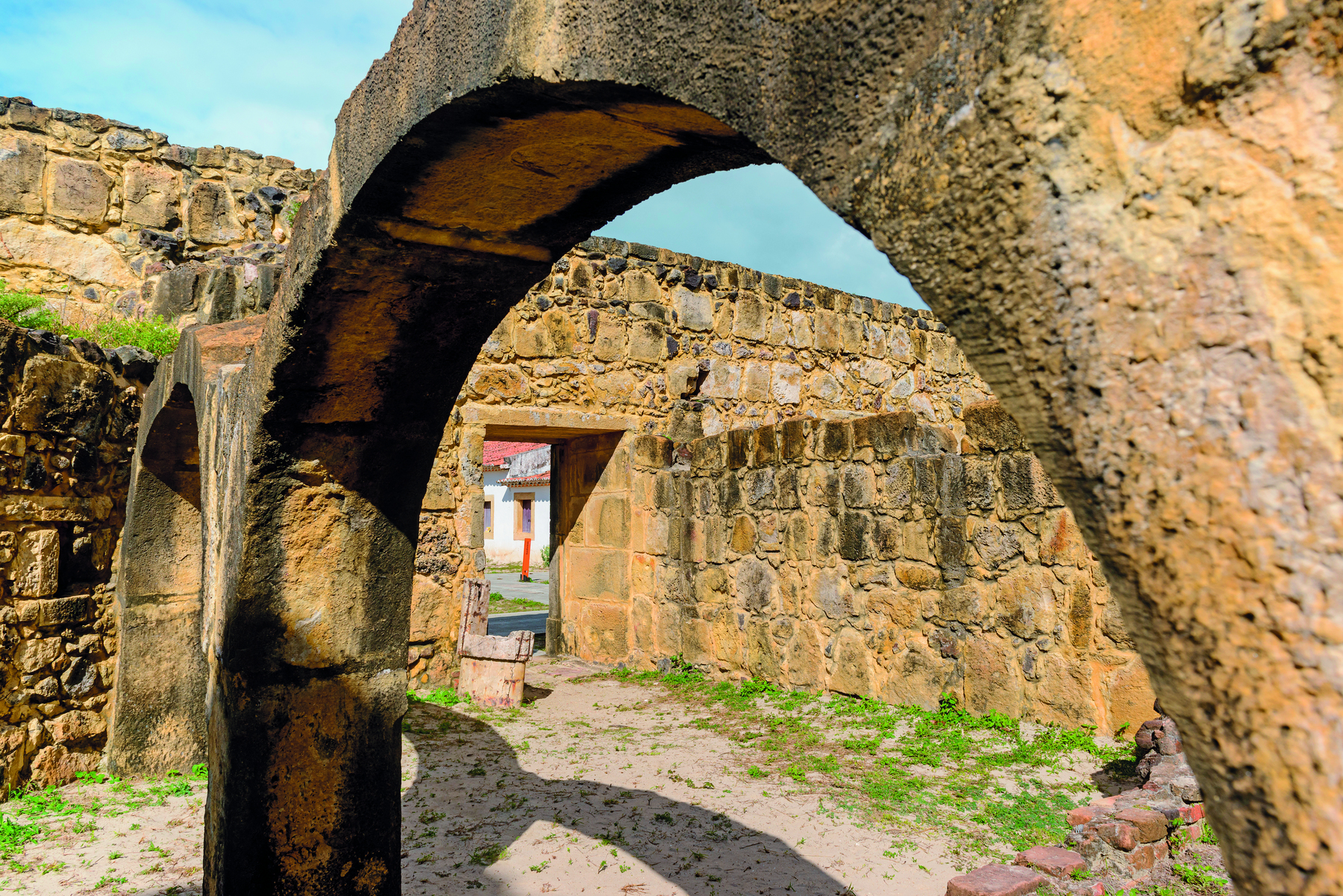 Fotografia. Uma construção de pedra em ruínas, com destaque para arcos com aberturas ao centro.