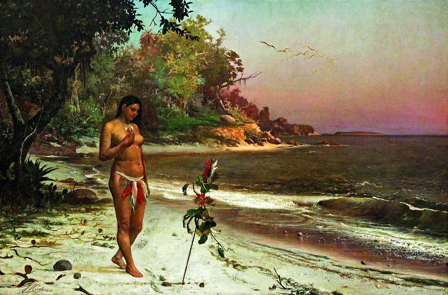 Pintura. Em uma praia, uma mulher indígena, com cabelos escuros, longos e lisos, com o peito desnudo, vestindo penas coloridas atadas a um cinto preso em sua cintura. Ela está em pé, sobre uma faixa de areia branca à margem de águas verdes. Em segundo plano, vegetação densa.