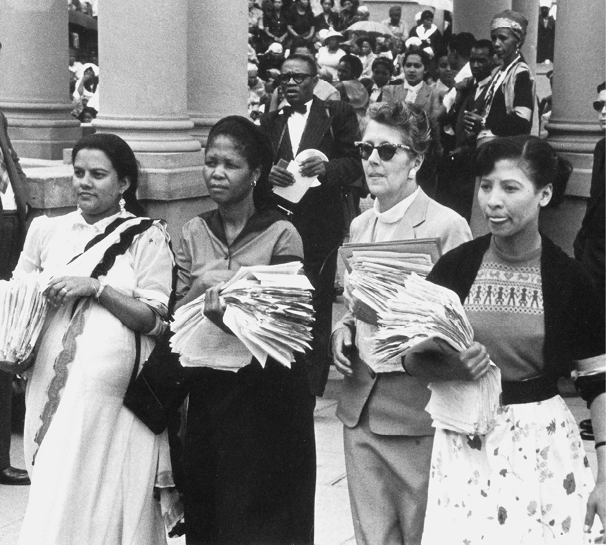 Fotografia em preto e branco. Quatro mulheres lado a lado, portando folhetos em suas mãos.