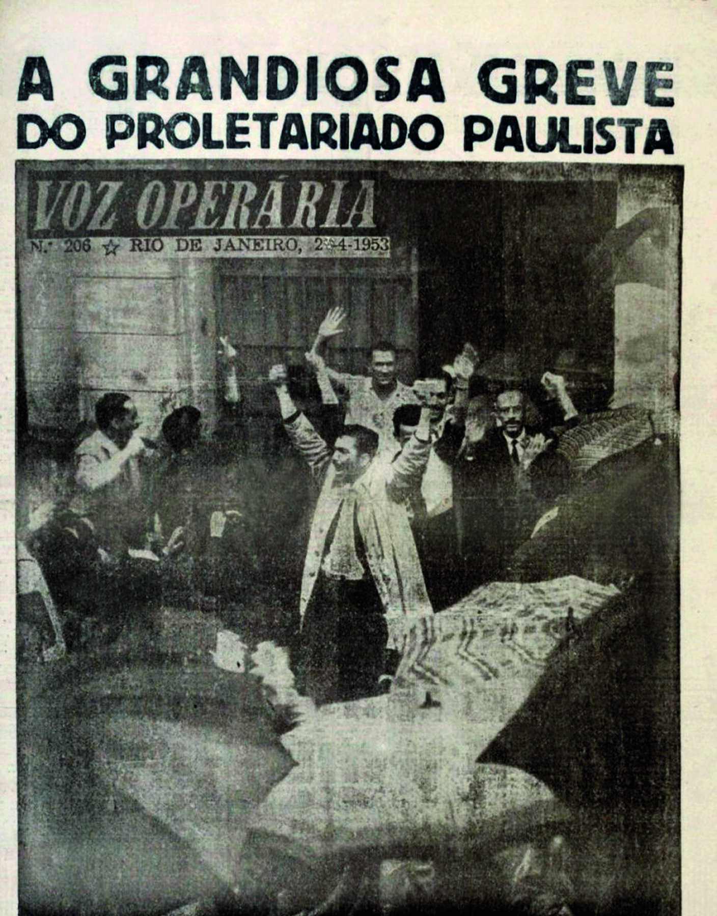 Fotografia em preto e branco. Capa de um jornal com a manchete: 'A grandiosa greve do proletariado paulista'. Ao centro, um grupo de homens aglomerados, com os braços e mãos ao alto.