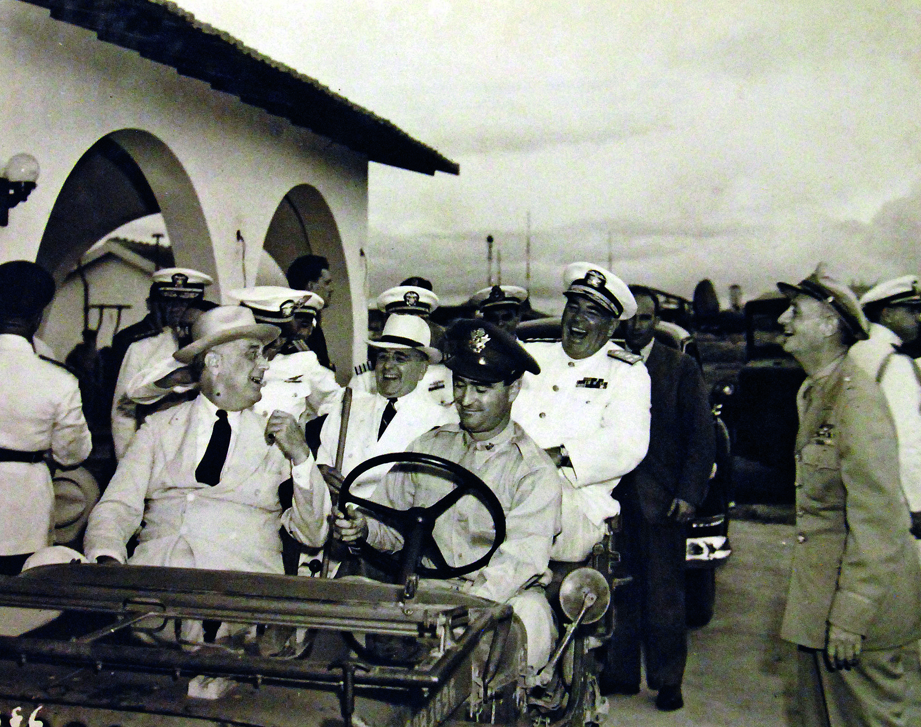 Fotografia em preto e branco. Um grupo de homens sobre um veículo antigo, alguns vestindo paletós, outros fardados.
