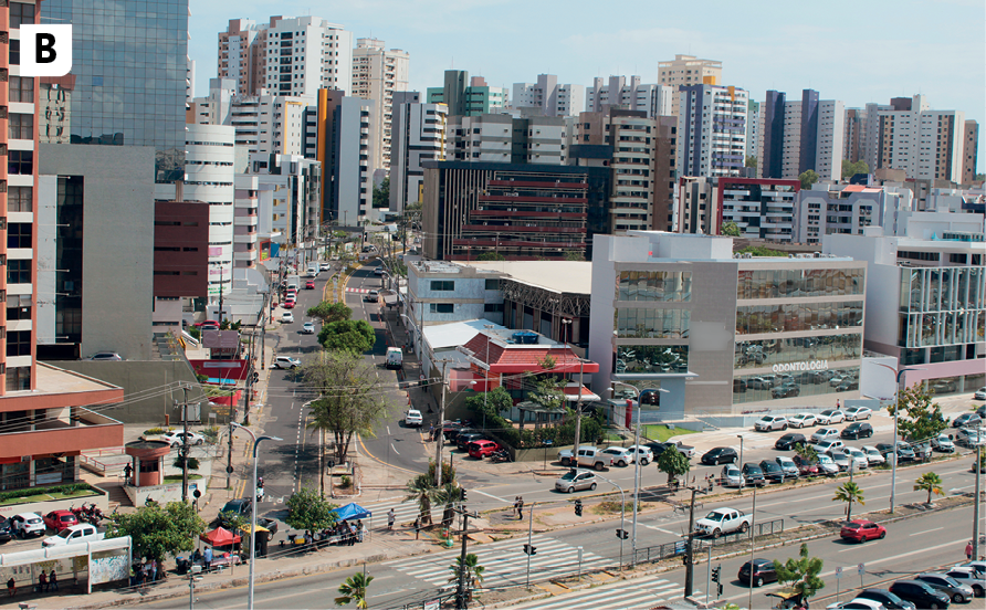 Fotografia B. Vista de uma área com muitos prédios de tamanhos e formas variadas, com ruas asfaltadas, muitos carros e poucas árvores.