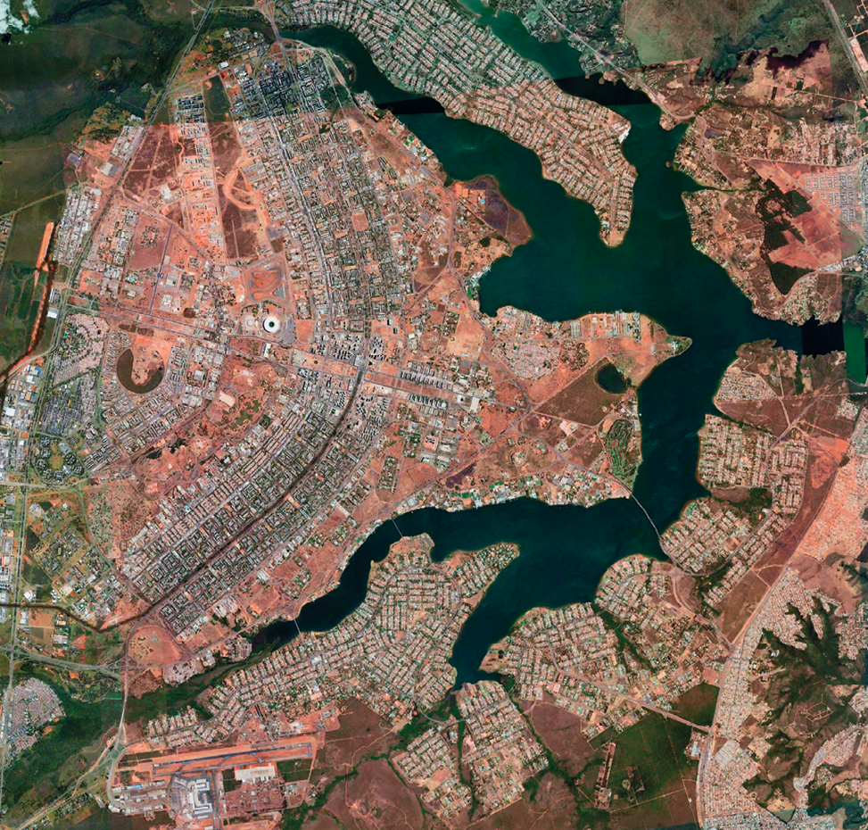 Imagem de satélite. Cidade de Brasília. Vista vertical da cidade de Brasília, com áreas com muitas construções, vias de circulação, um lago formado de diversos "braços" (ou canais) entre a área construída e alguns espaços de terra.