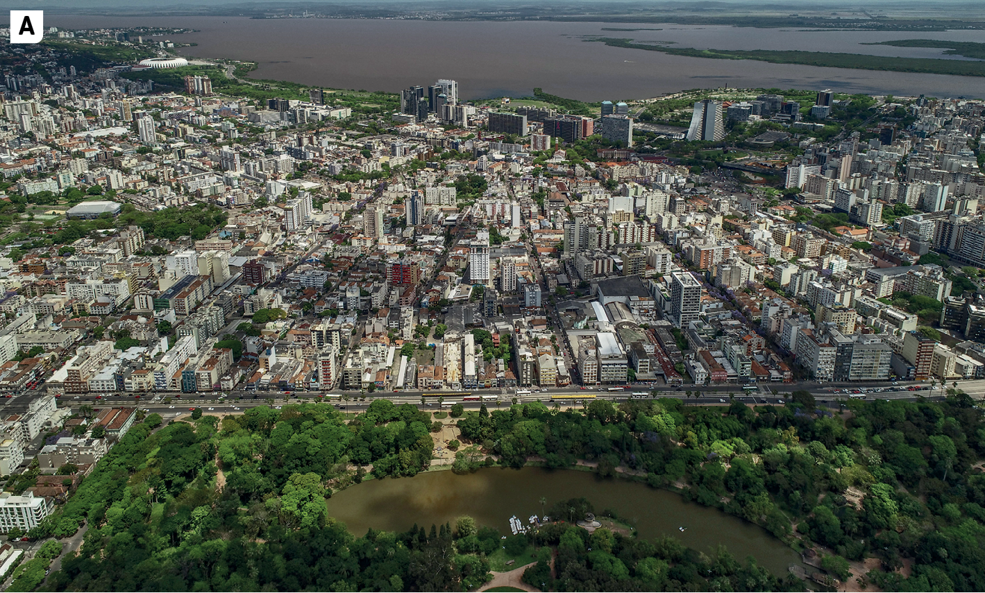 Fotografia A. Vista do alto de uma cidade. Na parte de baixo da imagem, uma área com vegetação e um pequeno lago; no centro, ocupando a maior parte da fotografia, muitos edifícios altos de vários andares; na parte de cima, ao fundo, vista de um extenso corpo de água.