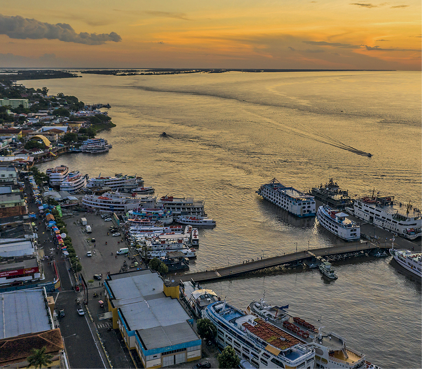 Fotografia. Vista do alto de parte da orla do Rio Amazonas e do porto do município de Parintins, com muitas embarcações.