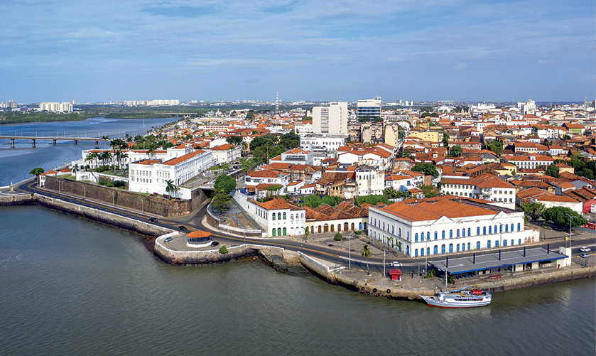 Fotografia. O centro histórico de São Luís com muitas construções históricas, cercado pelo mar, com uma embarcação nele.