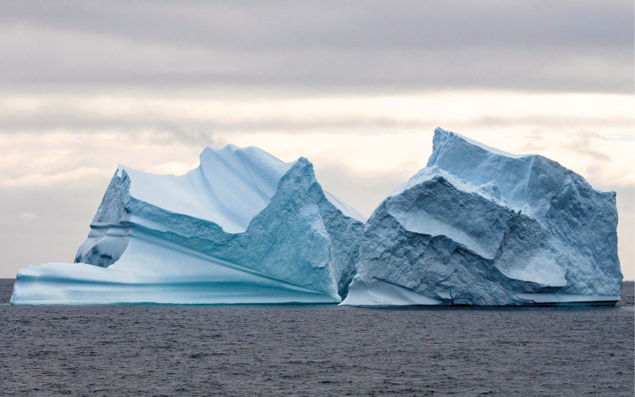 Fotografia. Vista frontal de um iceberg sobre mar.