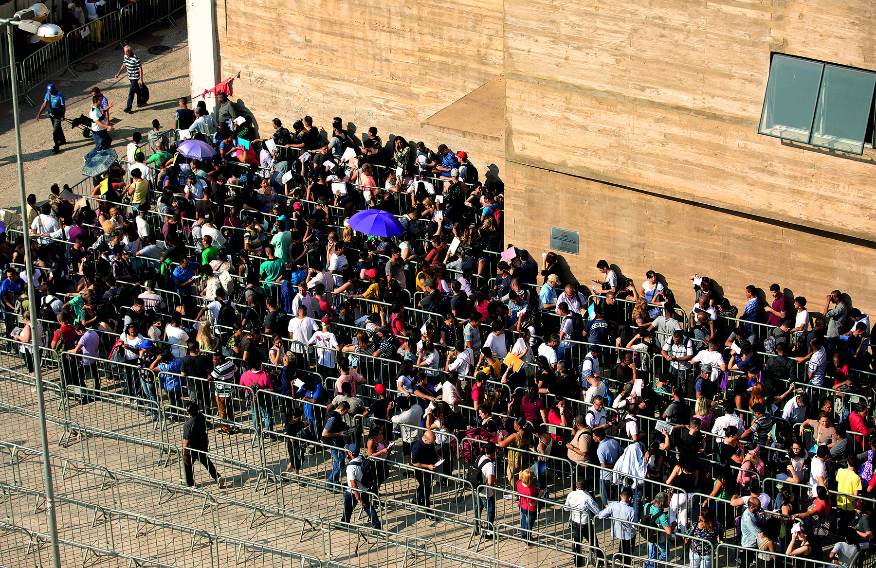 Fotografia. Vista do alto de diversas pessoas aglomeradas ao lado de uma construção.