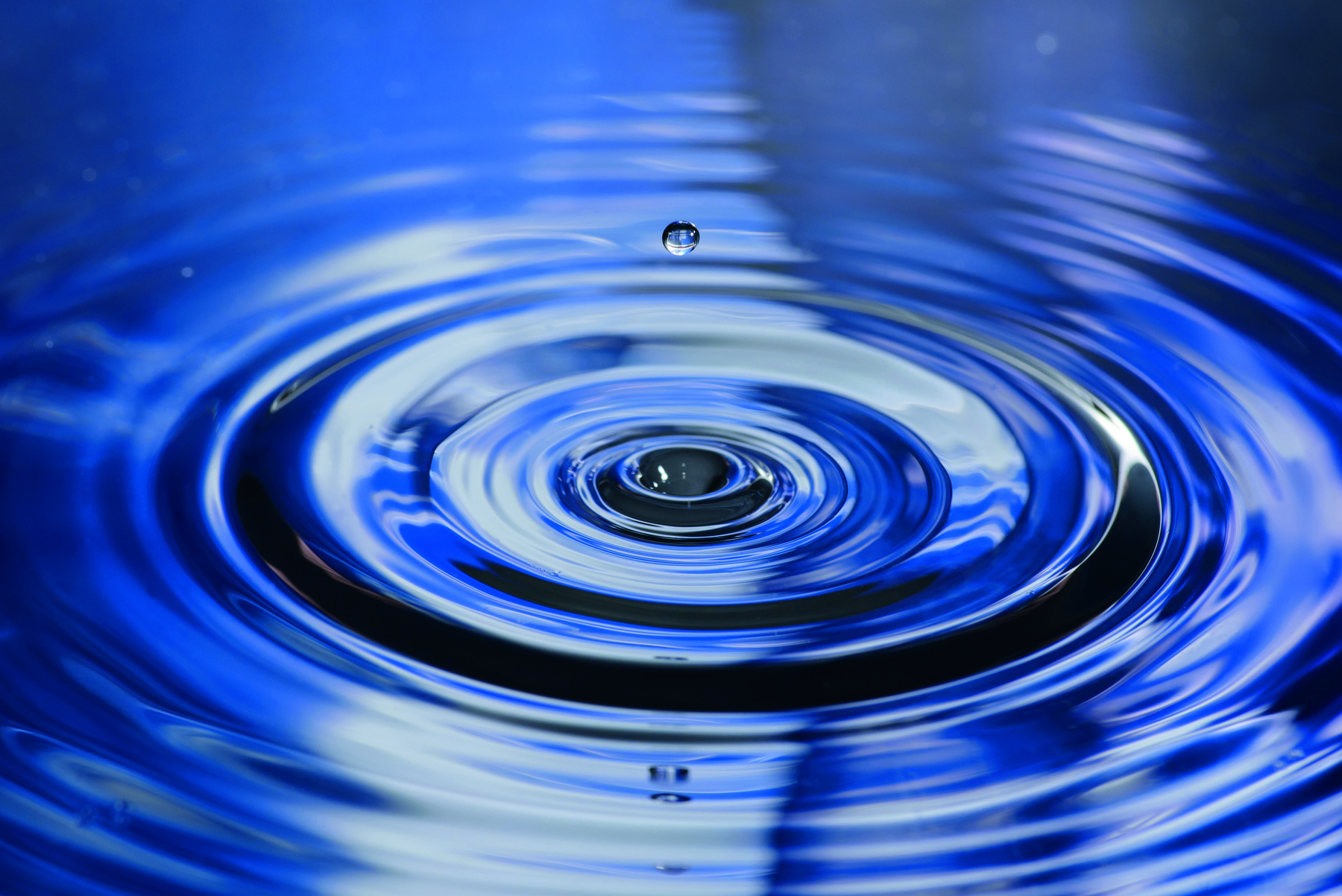 Fotografia. Pingo na superfície da água dando ideia de circunferências concêntricas.
