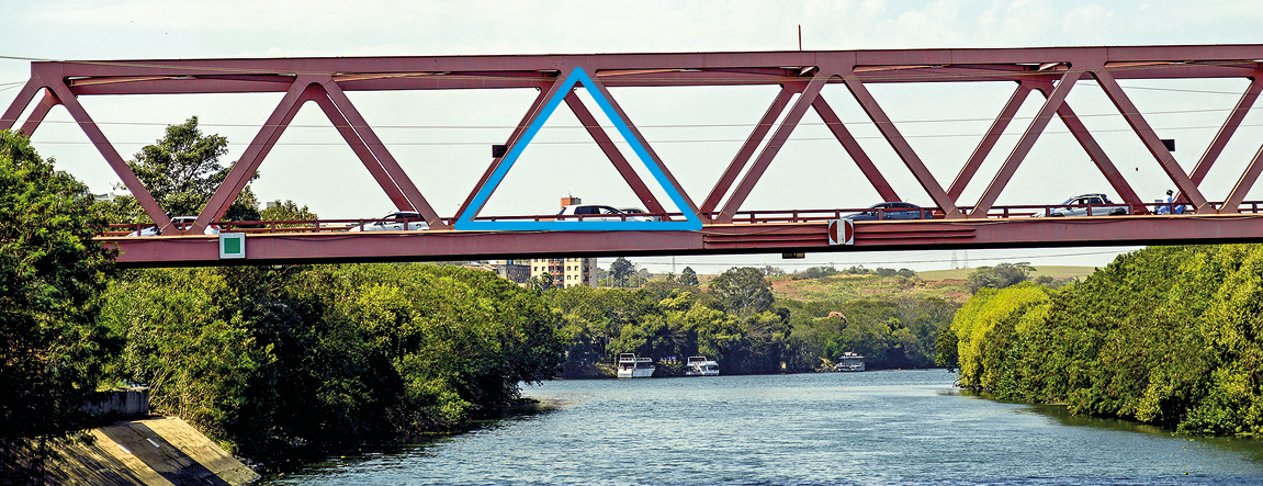 Fotografia. Estrutura metálica de uma ponte. Destaque para os formatos triangulares.