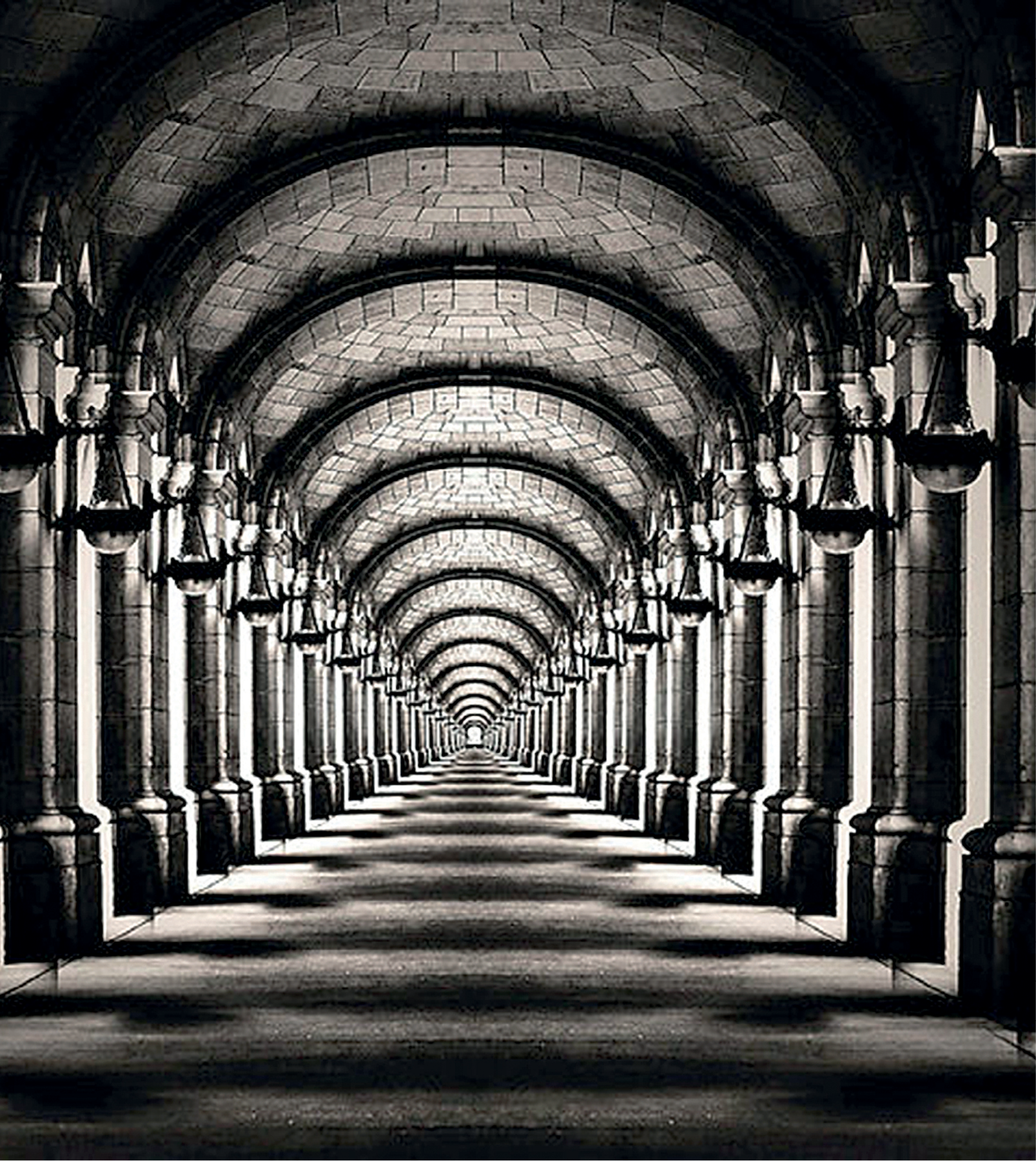 Fotografia em preto e branco. Vista do interior de estação composta por colunas nas laterais. O teto é arcado com blocos retangulares. Dando uma ideia  de profundidade e infinito.