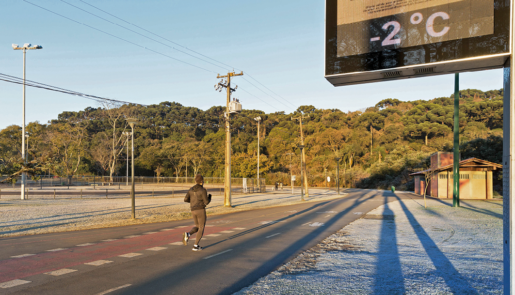 Fotografia. Pessoa correndo em pista de corrida. À direita, relógio digital marcando menos 2 graus Celsius.