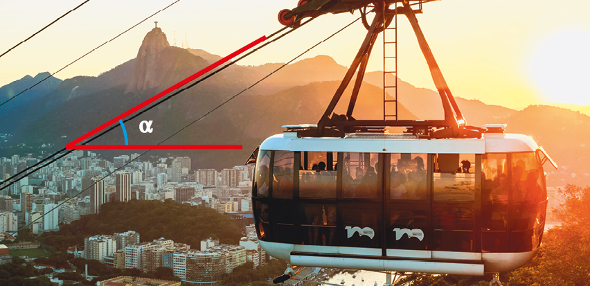 Fotografia. Destaque do alto de bondinho do teleférico com ângulo alfa entre os cabos e a vista lateral do bondinho. Ao fundo, sol entre morros. Abaixo, cidade do Rio de Janeiro.
