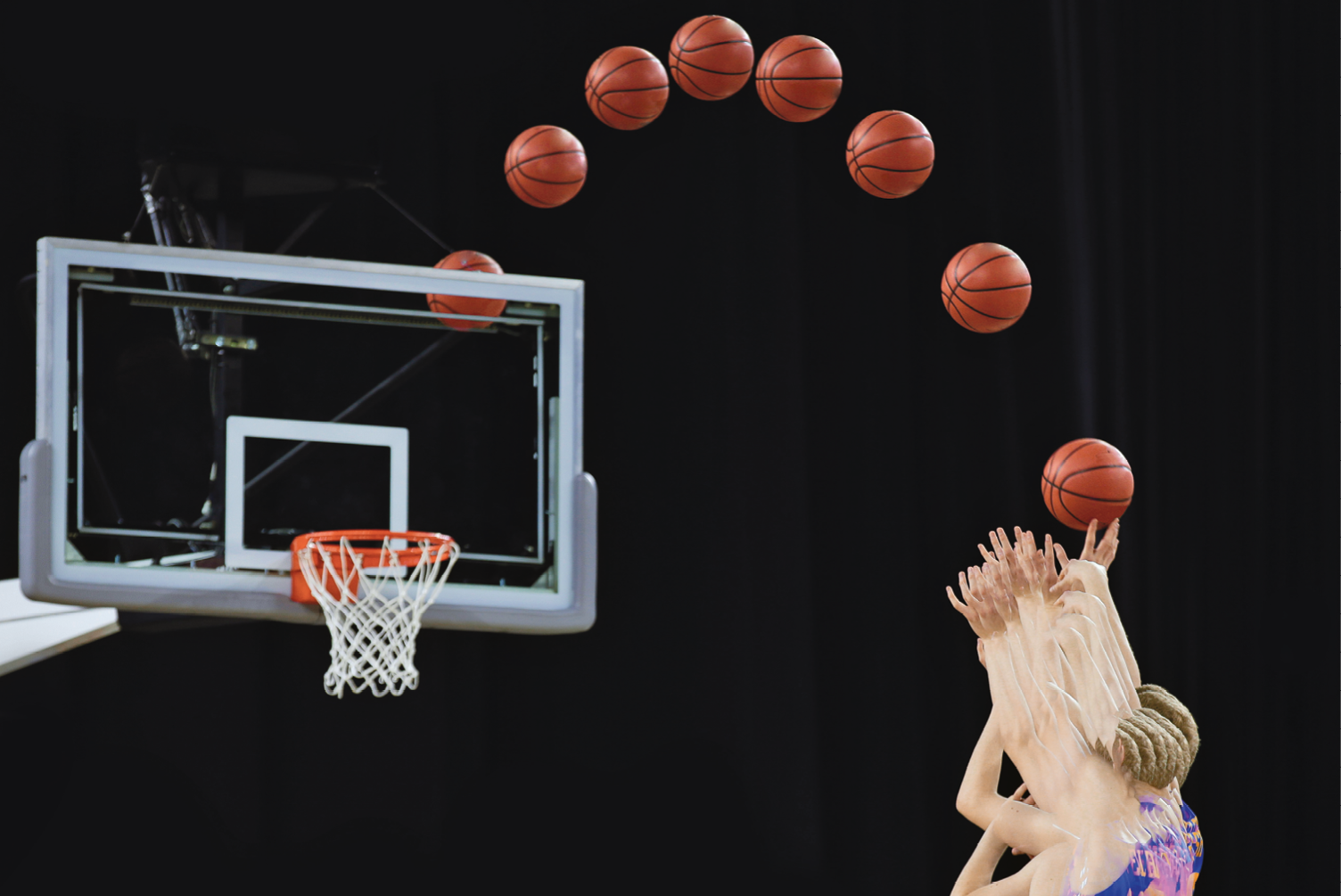 Fotografia. Destaque para as mãos de uma pessoa que lança uma bola de basquete em direção à cesta. A trajetória percorrida pela bola até chegar na cesta é registrada de tempo em tempo, formando uma parábola.