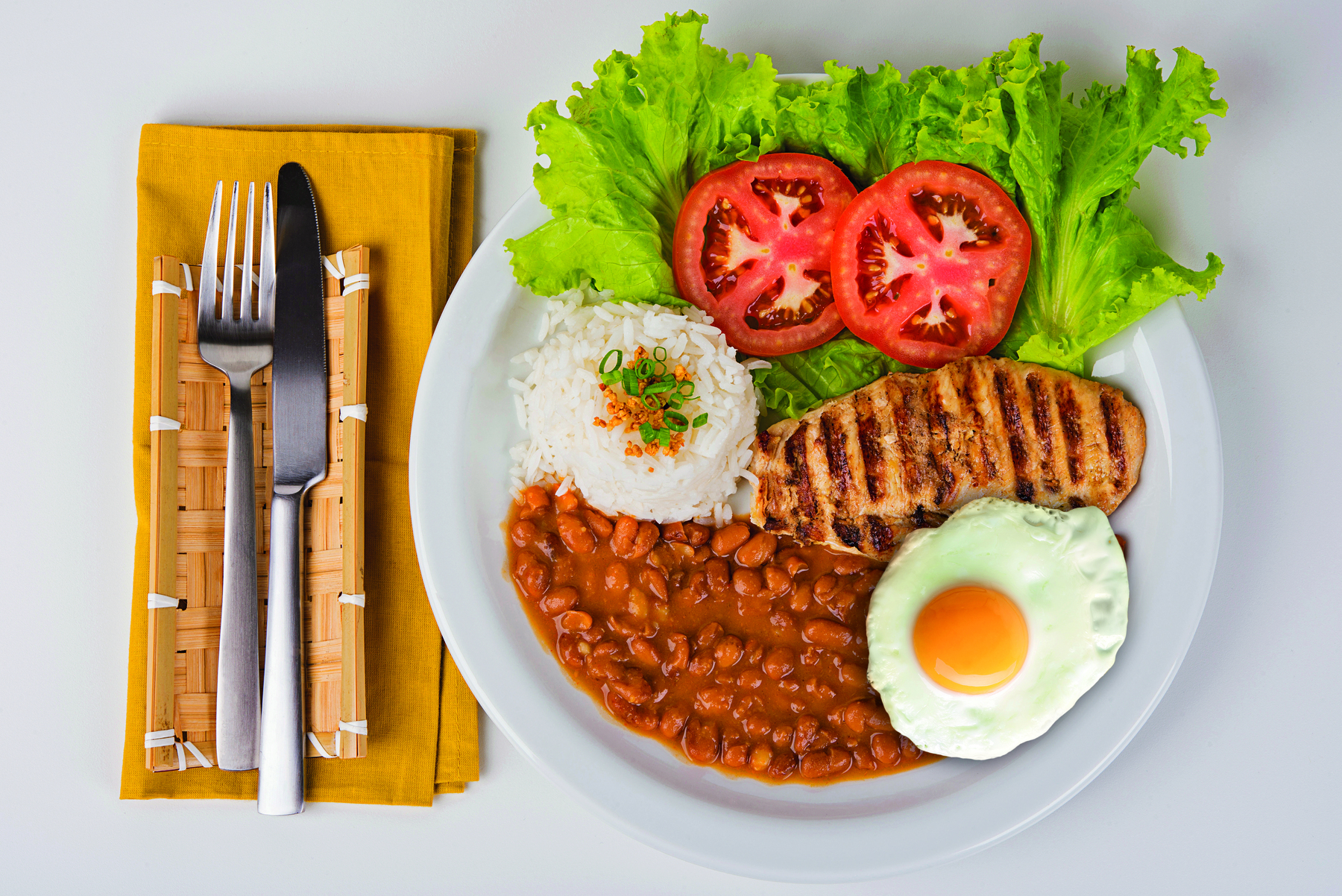 Fotografia. Um prato branco com arroz, feijão, filé de frango, ovo frito e salada de alface com tomate.