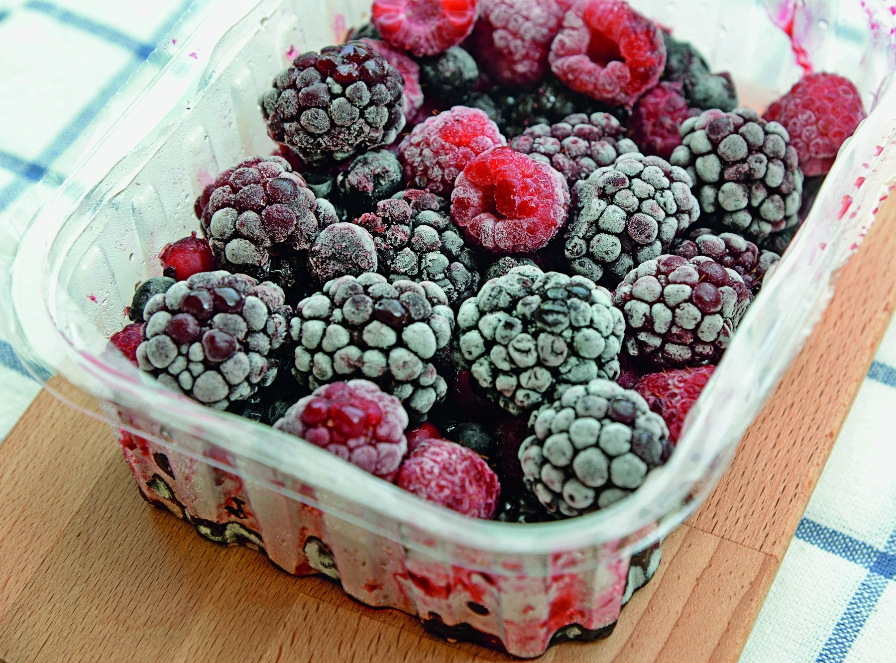 Fotografia. Uma vasilha com frutas roxas e frutas vermelhas congeladas.