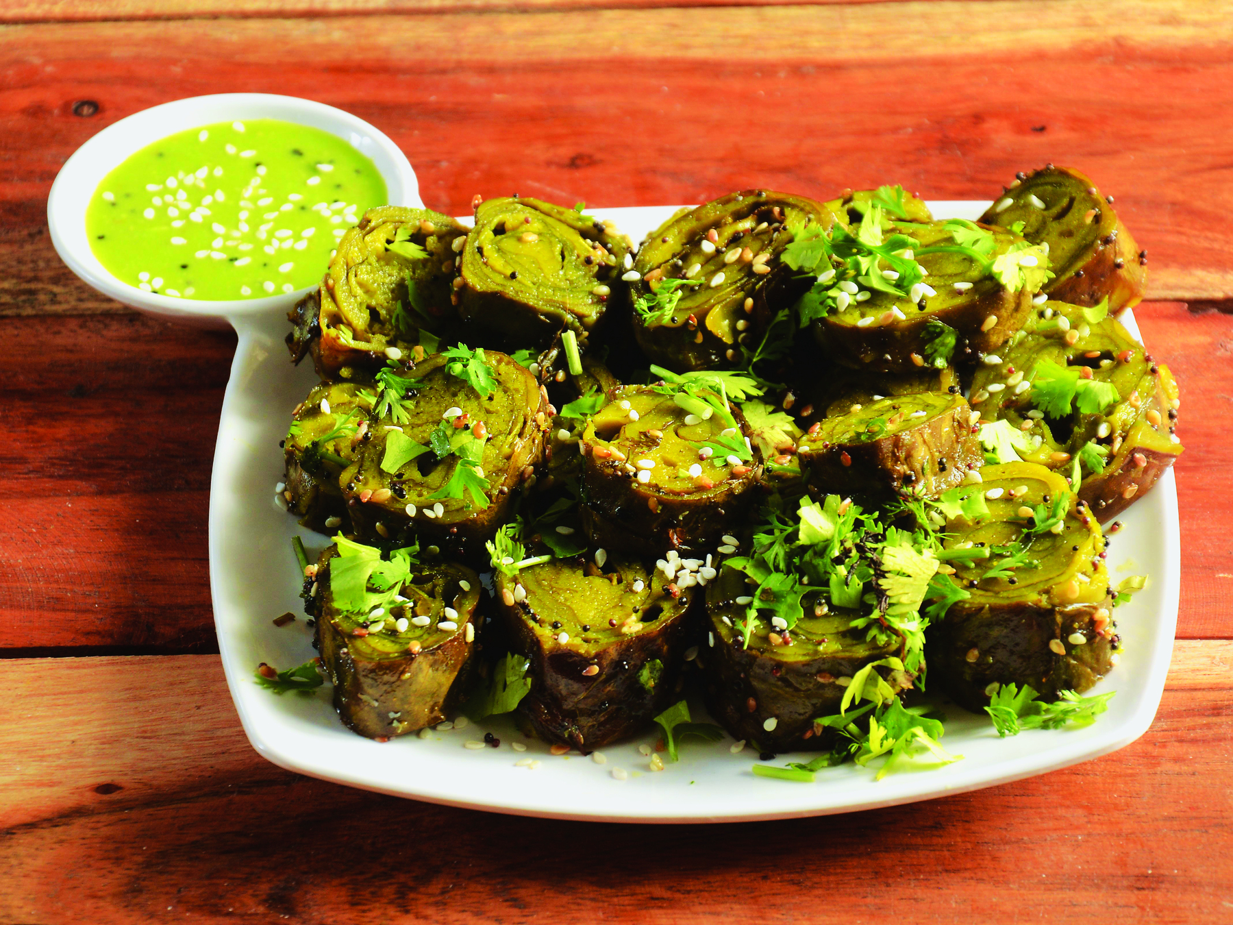 Fotografia. Um prato com patra,  pedaços circulares de uma comida marrom salpicada com pedaços de folhas verdes.