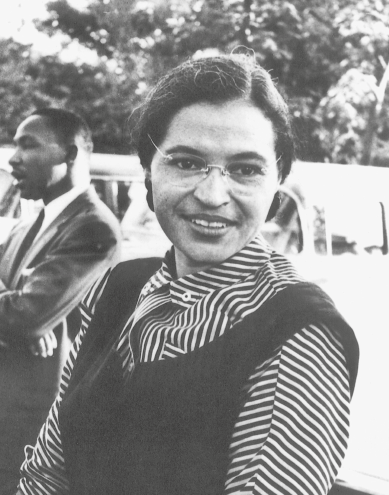 Fotografia. Retrato em preto e branco de Rosa Parks, uma mulher negra, cabelo escuro penteado para o lado, de sobrancelhas finas, usando camisa listrada preta e branca e colete preto. Ela está sorrindo.