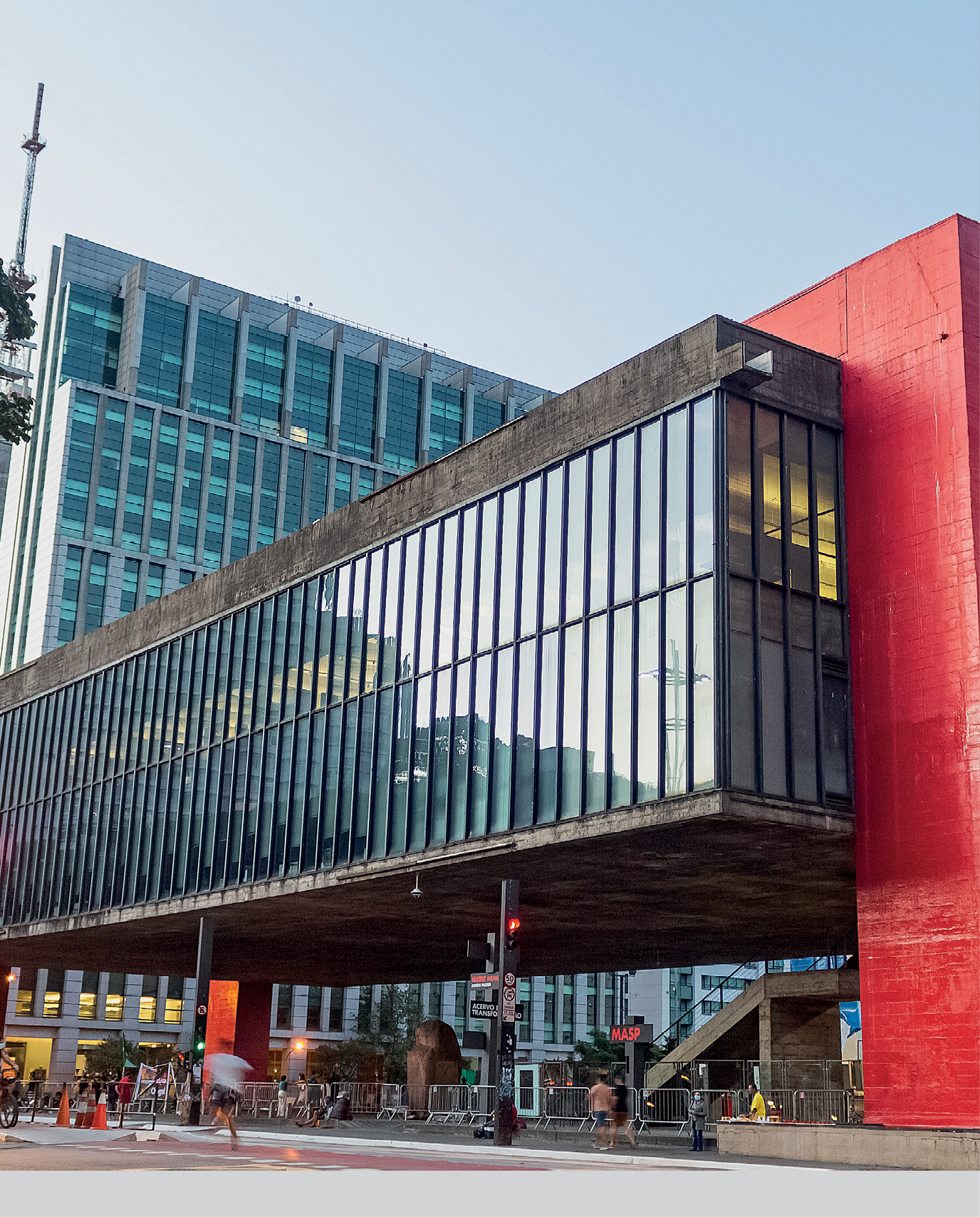 Fotografia. Museu de Arte de São Paulo. Um prédio cinza e vermelho em formato retangular na horizontal com janelas em vidro transparente.